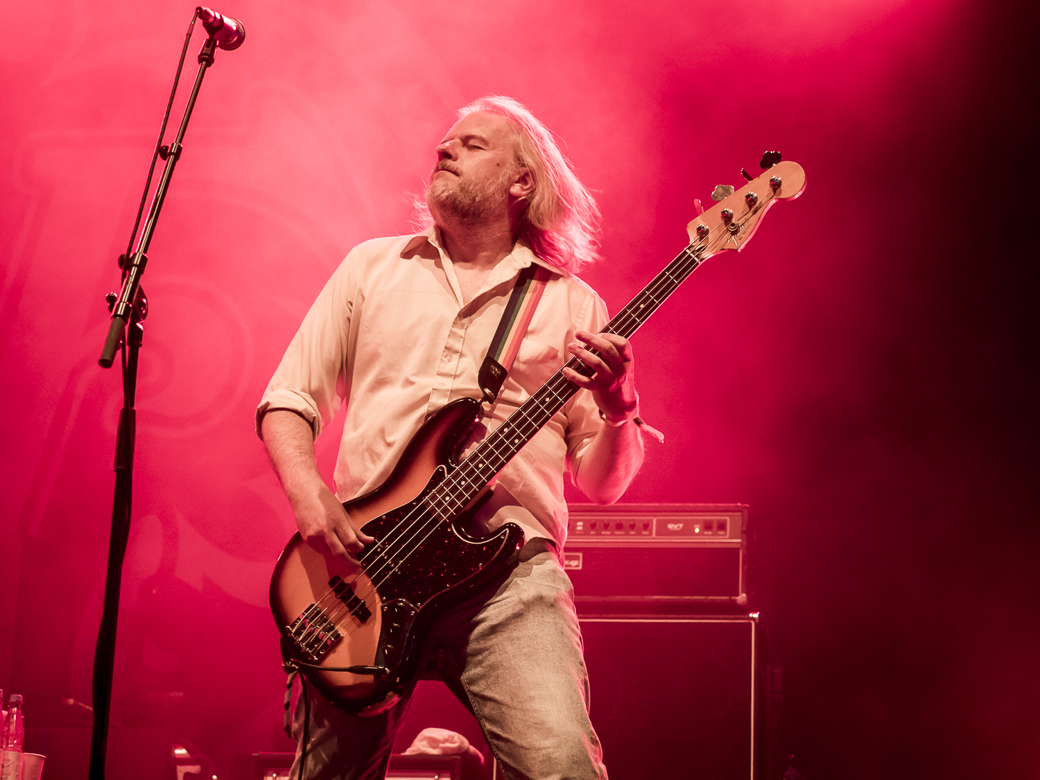 Ein Bassist spielt auf einer Bühne mit einer roten Hintergrundbeleuchtung während eines Live-Konzerts.