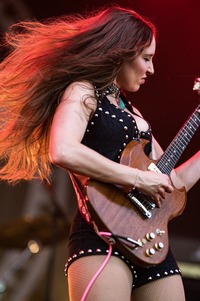 Frau mit langen, fließenden Haaren, die leidenschaftlich eine E-Gitarre auf der Bühne spielt, während sie energiegeladen und fokussiert aussieht.